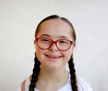 Child with Down syndrome, pigtails and glasses smiling